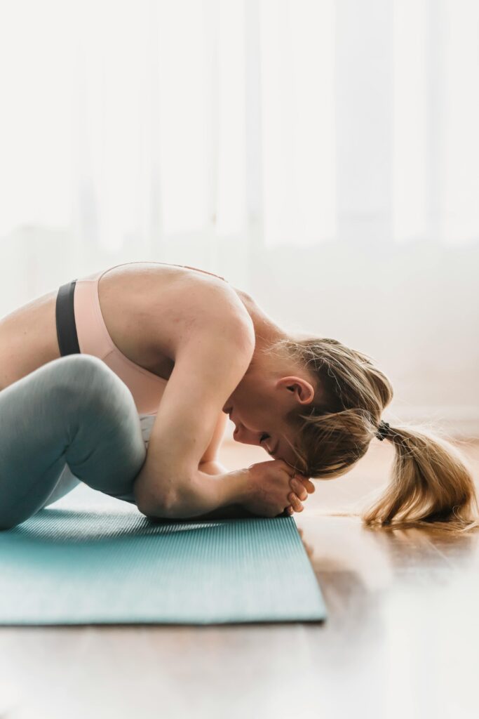 pexels-photo-6454108-6454108 Side view of focused young fit woman with long blond hair in sportswear stretching thighs while doing Baddha Konasana B yoga pose with closed eyes in sunny studio